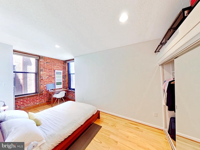 bedroom featuring a closet, a textured ceiling, brick wall, and light hardwood / wood-style flooring