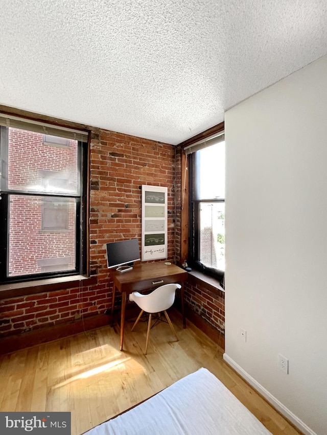 unfurnished office with a textured ceiling, light hardwood / wood-style floors, and brick wall