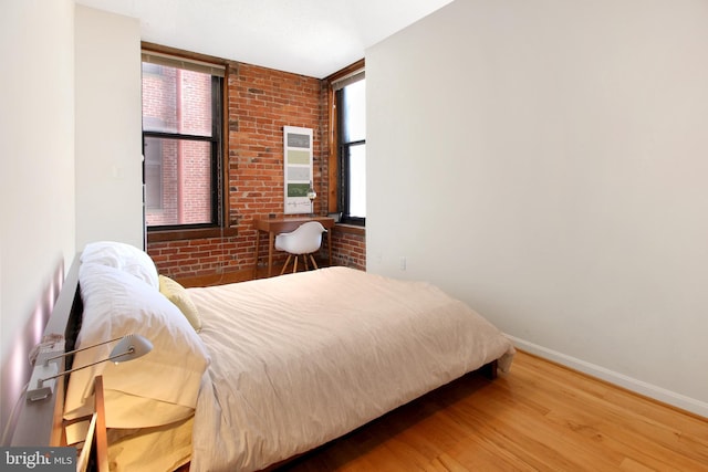 bedroom with hardwood / wood-style flooring and brick wall