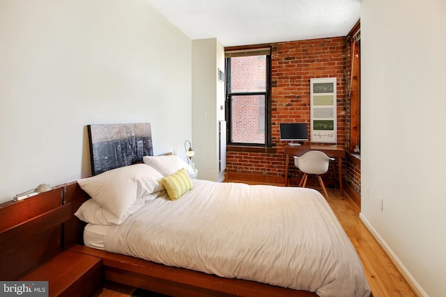 bedroom with hardwood / wood-style floors, a textured ceiling, and brick wall