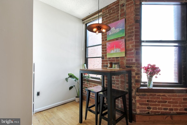 dining area featuring light hardwood / wood-style flooring, brick wall, and a textured ceiling