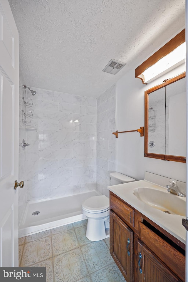 bathroom with toilet, a textured ceiling, tiled shower, and vanity