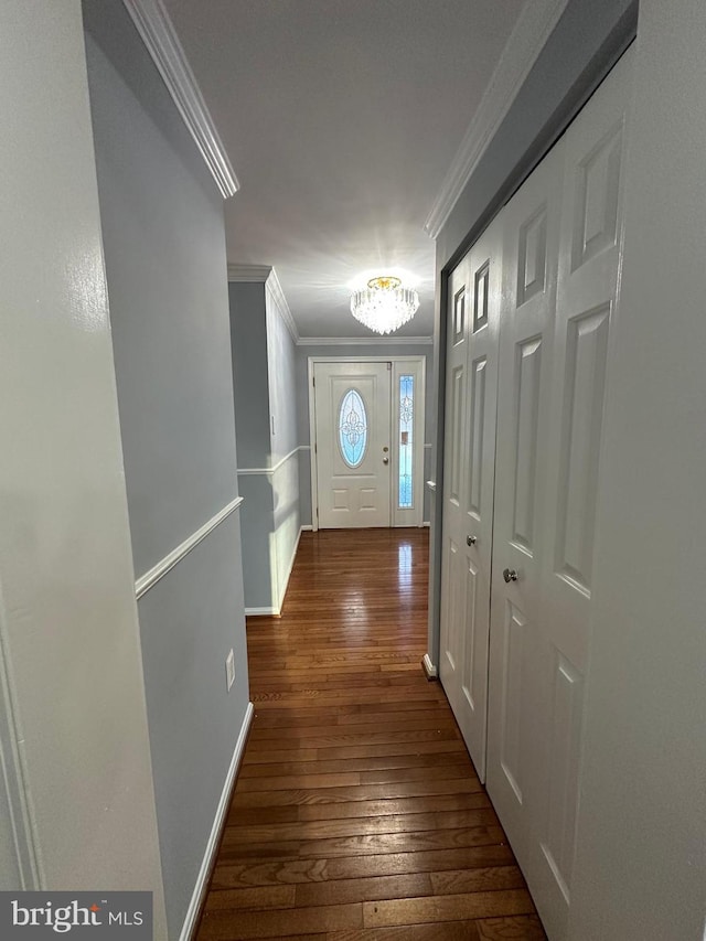 entryway featuring dark wood-type flooring, crown molding, and a chandelier