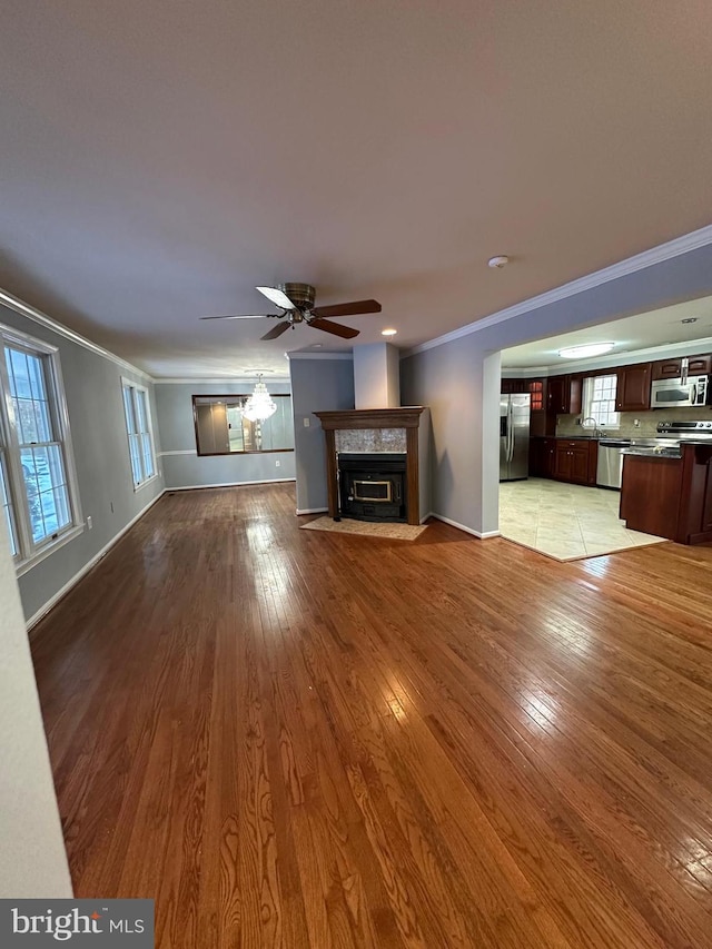 unfurnished living room featuring light wood-type flooring, ceiling fan, ornamental molding, and plenty of natural light