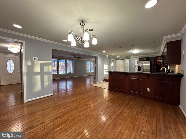 kitchen featuring hanging light fixtures, appliances with stainless steel finishes, dark wood-type flooring, ornamental molding, and ceiling fan with notable chandelier