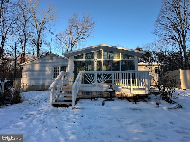 snow covered property with a wooden deck and a sunroom