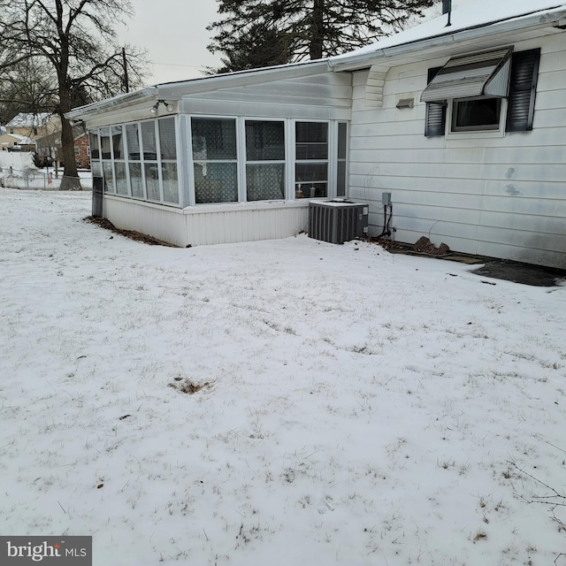 snow covered house featuring central AC unit and a sunroom