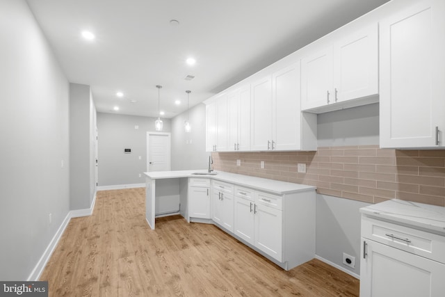 kitchen featuring kitchen peninsula, sink, pendant lighting, white cabinets, and light hardwood / wood-style floors