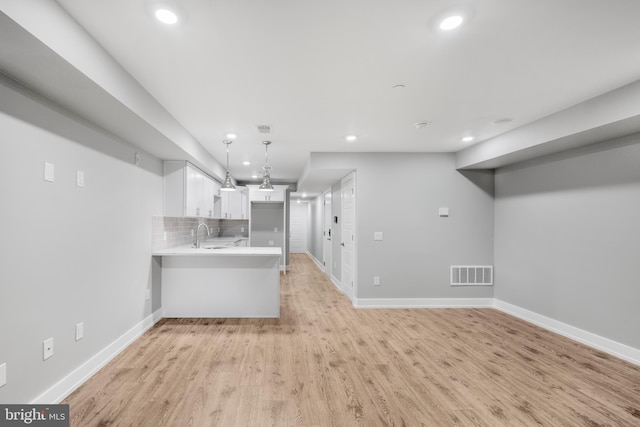 interior space featuring tasteful backsplash, kitchen peninsula, light hardwood / wood-style floors, decorative light fixtures, and white cabinets