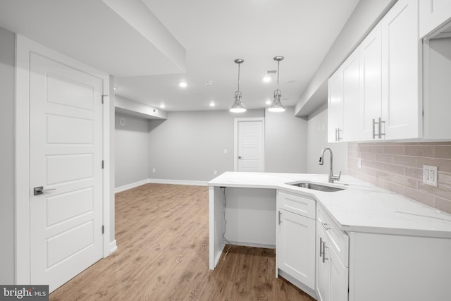 kitchen with decorative light fixtures, white cabinetry, sink, and light hardwood / wood-style flooring