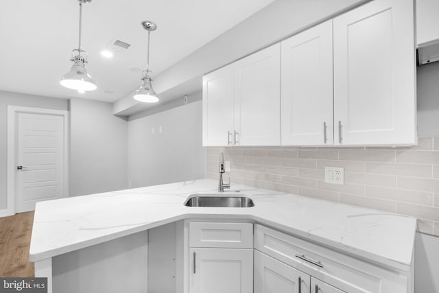 kitchen featuring pendant lighting, light stone countertops, white cabinetry, and sink