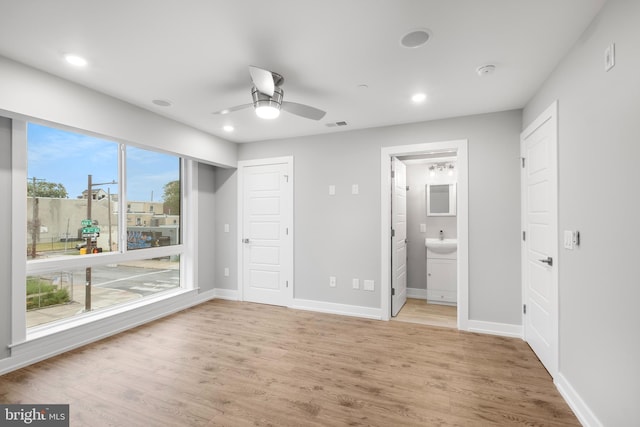 unfurnished bedroom with connected bathroom, ceiling fan, hardwood / wood-style floors, and multiple windows