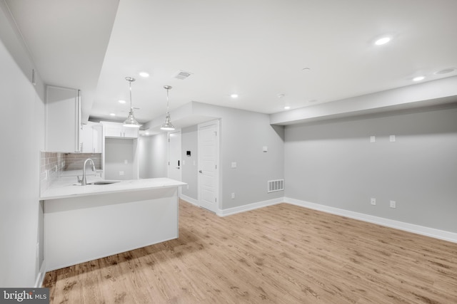 kitchen with kitchen peninsula, backsplash, sink, pendant lighting, and white cabinets