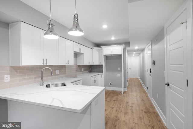 kitchen with pendant lighting, light stone counters, white cabinetry, and sink