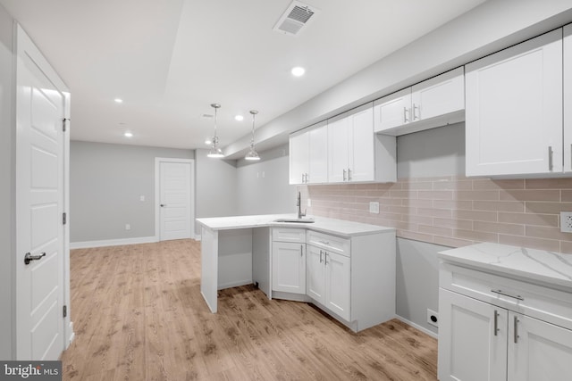 kitchen with kitchen peninsula, tasteful backsplash, sink, decorative light fixtures, and white cabinetry