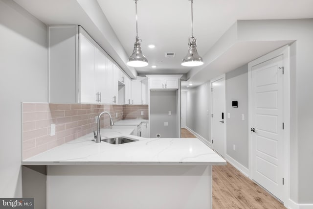 kitchen featuring decorative backsplash, light stone countertops, sink, white cabinetry, and hanging light fixtures