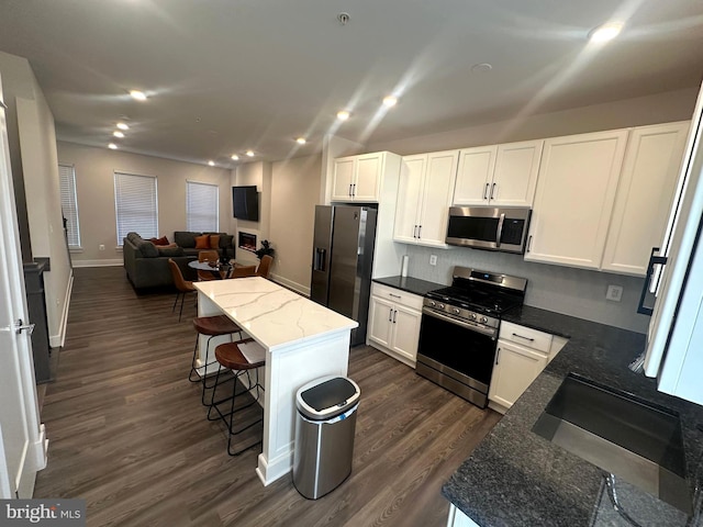 kitchen with a breakfast bar, dark stone counters, a kitchen island, white cabinetry, and stainless steel appliances