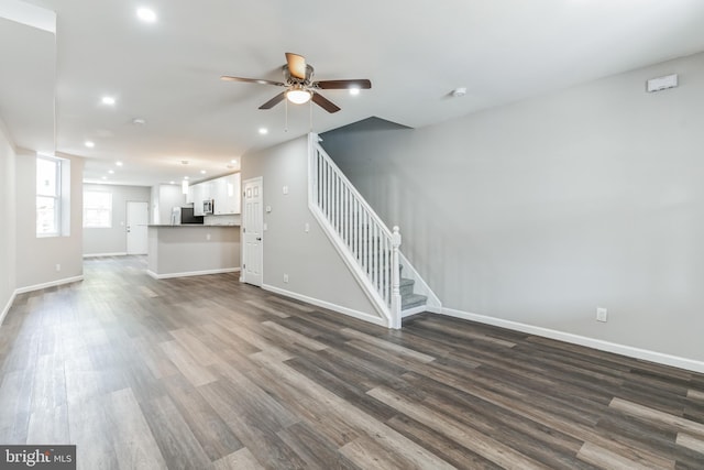 unfurnished living room featuring ceiling fan and dark wood-type flooring