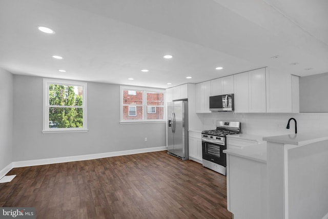 kitchen with kitchen peninsula, appliances with stainless steel finishes, tasteful backsplash, dark hardwood / wood-style floors, and white cabinetry