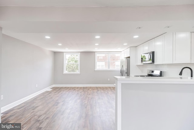 kitchen featuring white cabinetry, stainless steel appliances, tasteful backsplash, kitchen peninsula, and light wood-type flooring