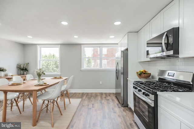 kitchen featuring white cabinets, decorative backsplash, stainless steel appliances, and light hardwood / wood-style flooring