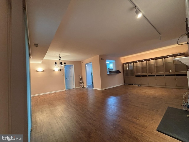 unfurnished living room featuring wood-type flooring, track lighting, and a notable chandelier