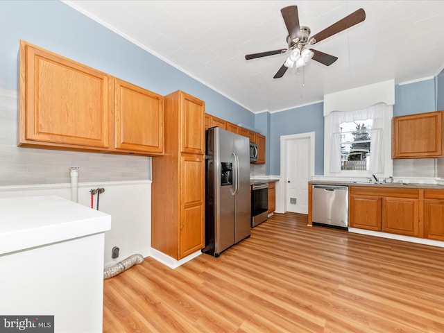 kitchen with ceiling fan, sink, light wood-type flooring, appliances with stainless steel finishes, and ornamental molding