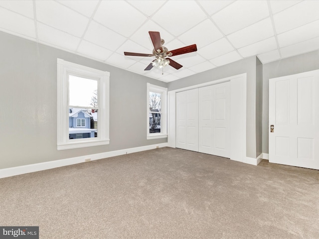 unfurnished bedroom with a paneled ceiling, ceiling fan, carpet floors, and a closet