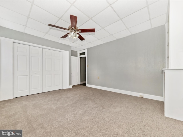 unfurnished bedroom featuring carpet flooring, a drop ceiling, a closet, and ceiling fan