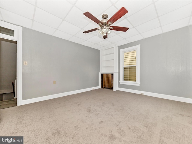 unfurnished living room featuring carpet flooring, ceiling fan, built in features, and a drop ceiling