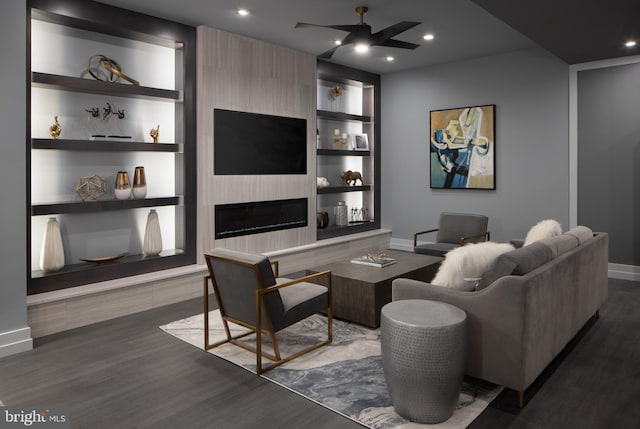 living room featuring built in shelves, dark hardwood / wood-style floors, ceiling fan, and a large fireplace