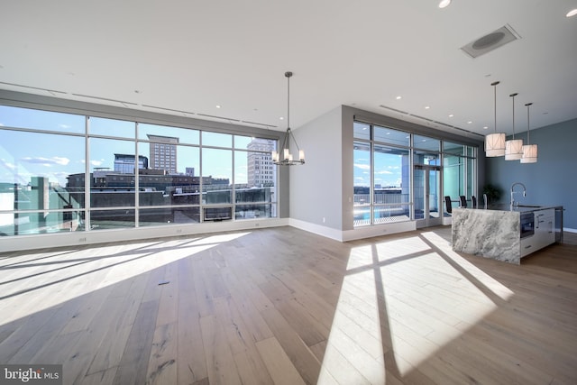 unfurnished living room with sink, expansive windows, a chandelier, and light wood-type flooring