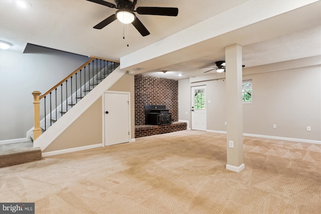 unfurnished living room featuring a wood stove, ceiling fan, and light colored carpet