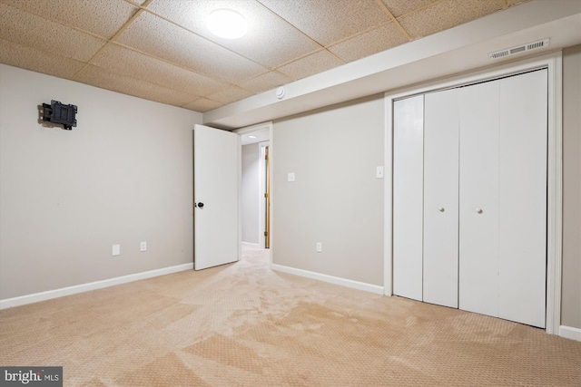 unfurnished bedroom featuring a paneled ceiling, light carpet, and a closet