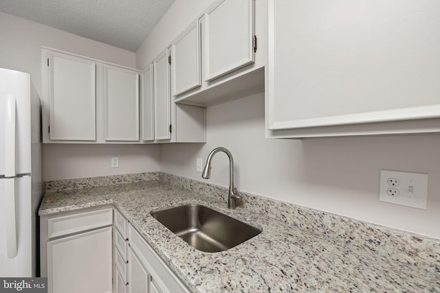 kitchen with white refrigerator, white cabinetry, sink, and a textured ceiling