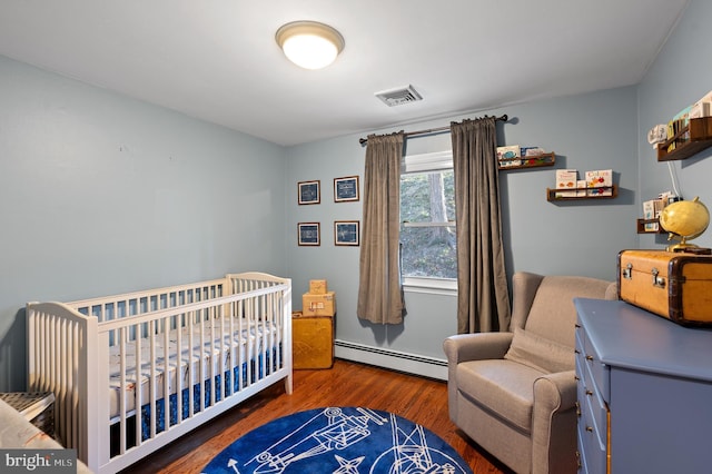 bedroom featuring a crib, baseboard heating, and dark wood-type flooring