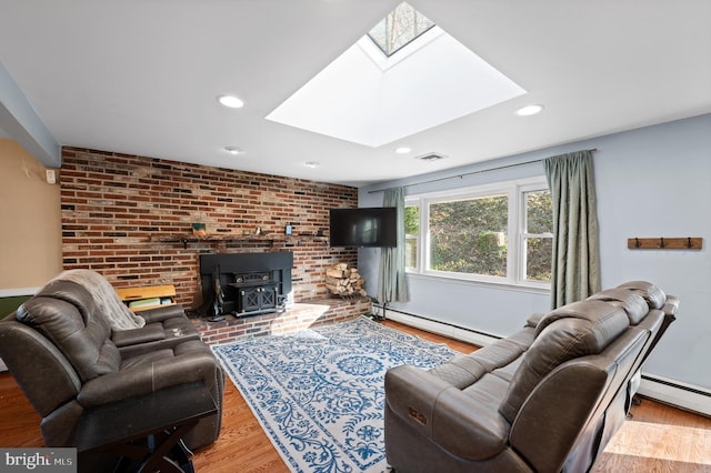 living room with a skylight, light hardwood / wood-style floors, brick wall, and a wood stove