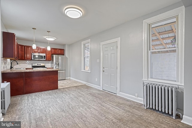 kitchen with kitchen peninsula, appliances with stainless steel finishes, backsplash, radiator, and sink