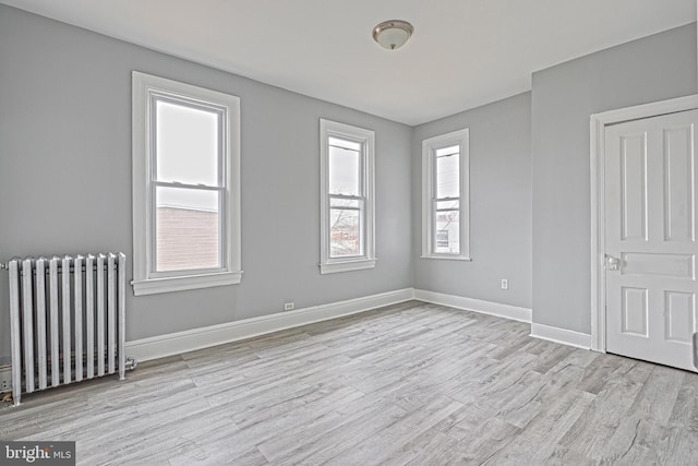 unfurnished room featuring radiator, a wealth of natural light, and light hardwood / wood-style floors