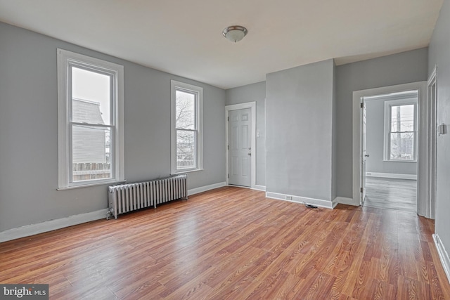 empty room with plenty of natural light, light wood-type flooring, and radiator heating unit