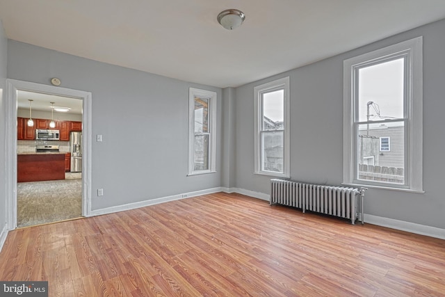 spare room with radiator heating unit and light hardwood / wood-style floors