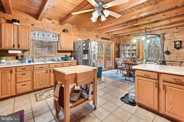 kitchen featuring stainless steel refrigerator with ice dispenser, wood ceiling, ceiling fan, wooden walls, and light tile patterned floors