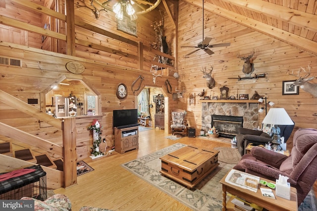 living room with beam ceiling, wooden walls, a fireplace, wood ceiling, and light wood-type flooring