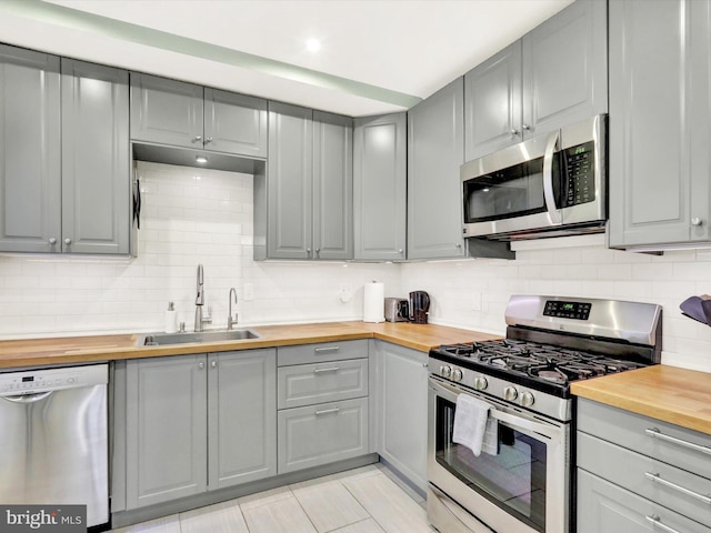 kitchen featuring sink, light tile patterned floors, wooden counters, and appliances with stainless steel finishes