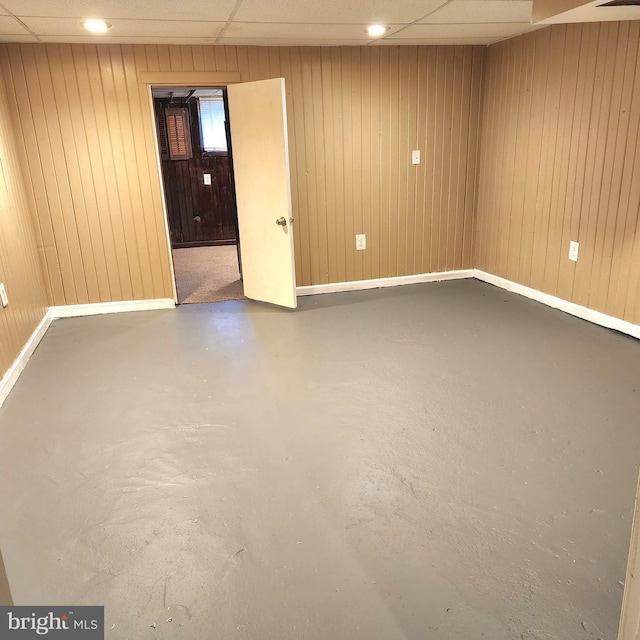 basement featuring wood walls and a drop ceiling