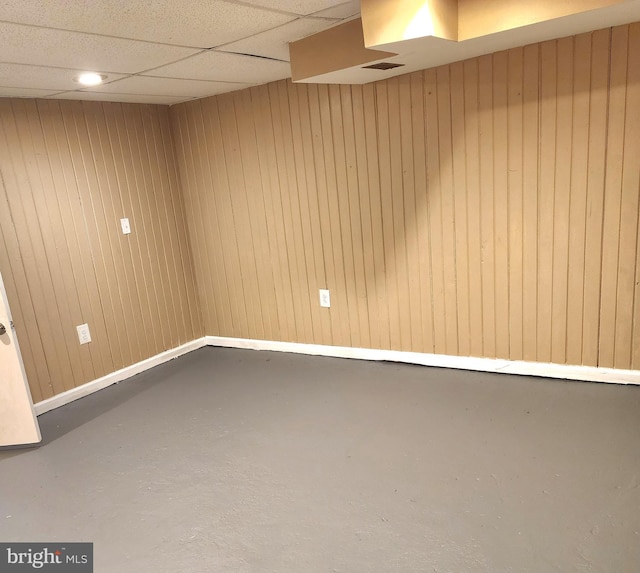 empty room featuring wood walls, a drop ceiling, and concrete floors