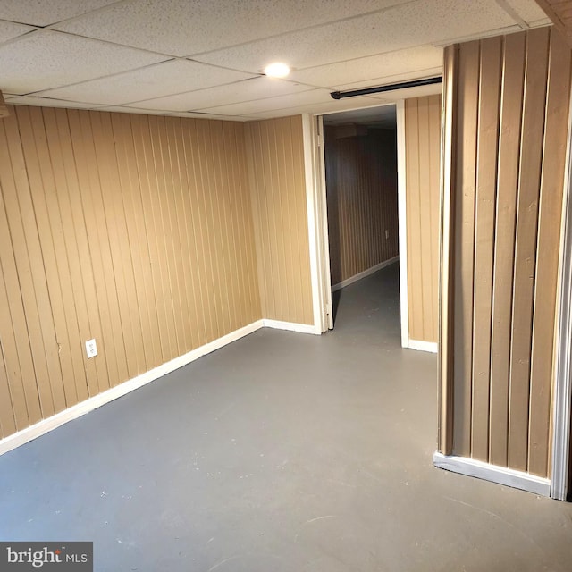 basement featuring a paneled ceiling and wooden walls