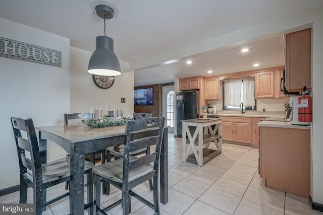 kitchen with light brown cabinets, black refrigerator, sink, light tile patterned floors, and decorative light fixtures