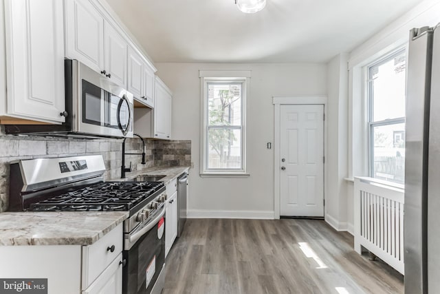 kitchen featuring white cabinets, sink, light hardwood / wood-style flooring, decorative backsplash, and appliances with stainless steel finishes