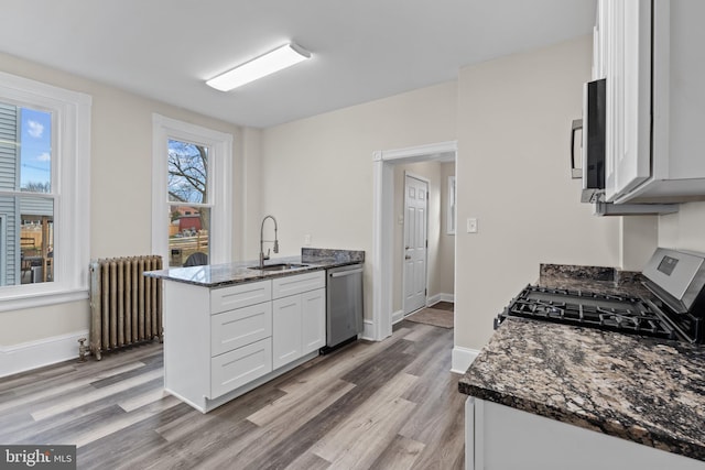 kitchen with white cabinetry, radiator heating unit, sink, stainless steel dishwasher, and dark stone countertops